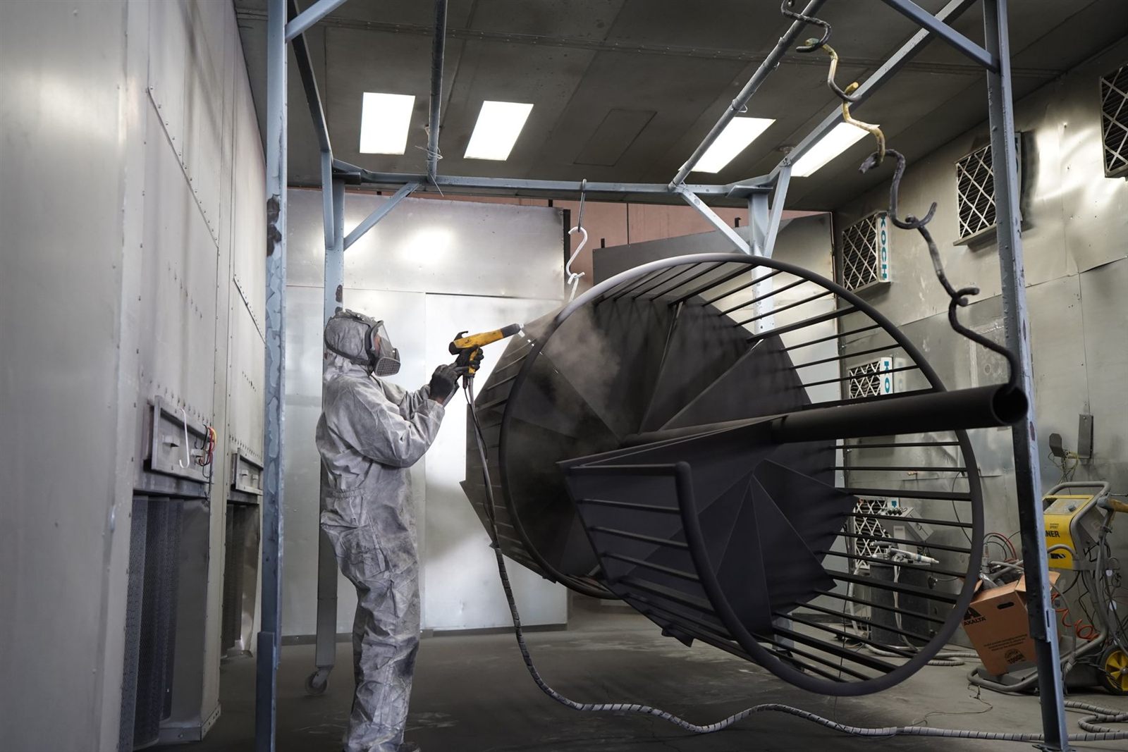 Technician applying powder coating in a controlled workshop booth